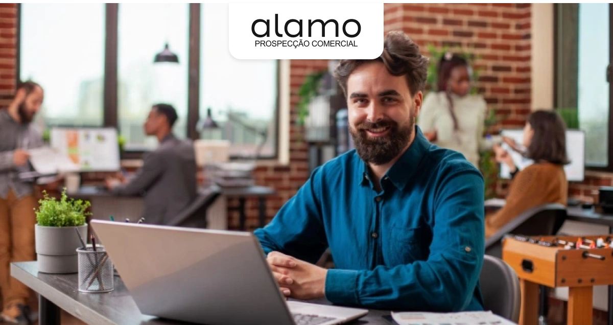 Profissional trabalhando em notebook em ambiente corporativo colaborativo, representando organização comercial e prospecção estratégica, com marca Alamo.
