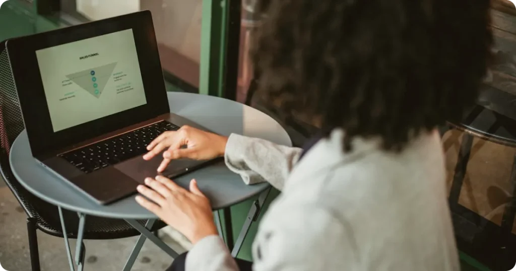 Profissional utilizando notebook em mesa, visualizando um funil de vendas na tela, indicando análise de processos comerciais e conversão.